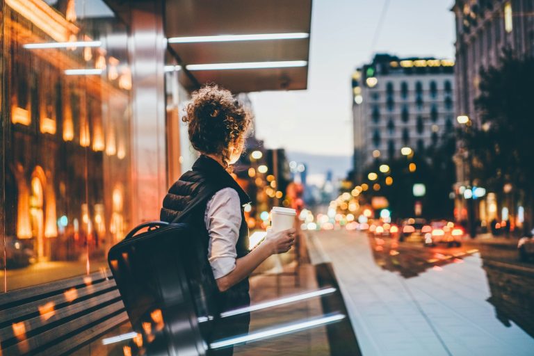 Businesswoman waiting for public transport and drinking coffee
